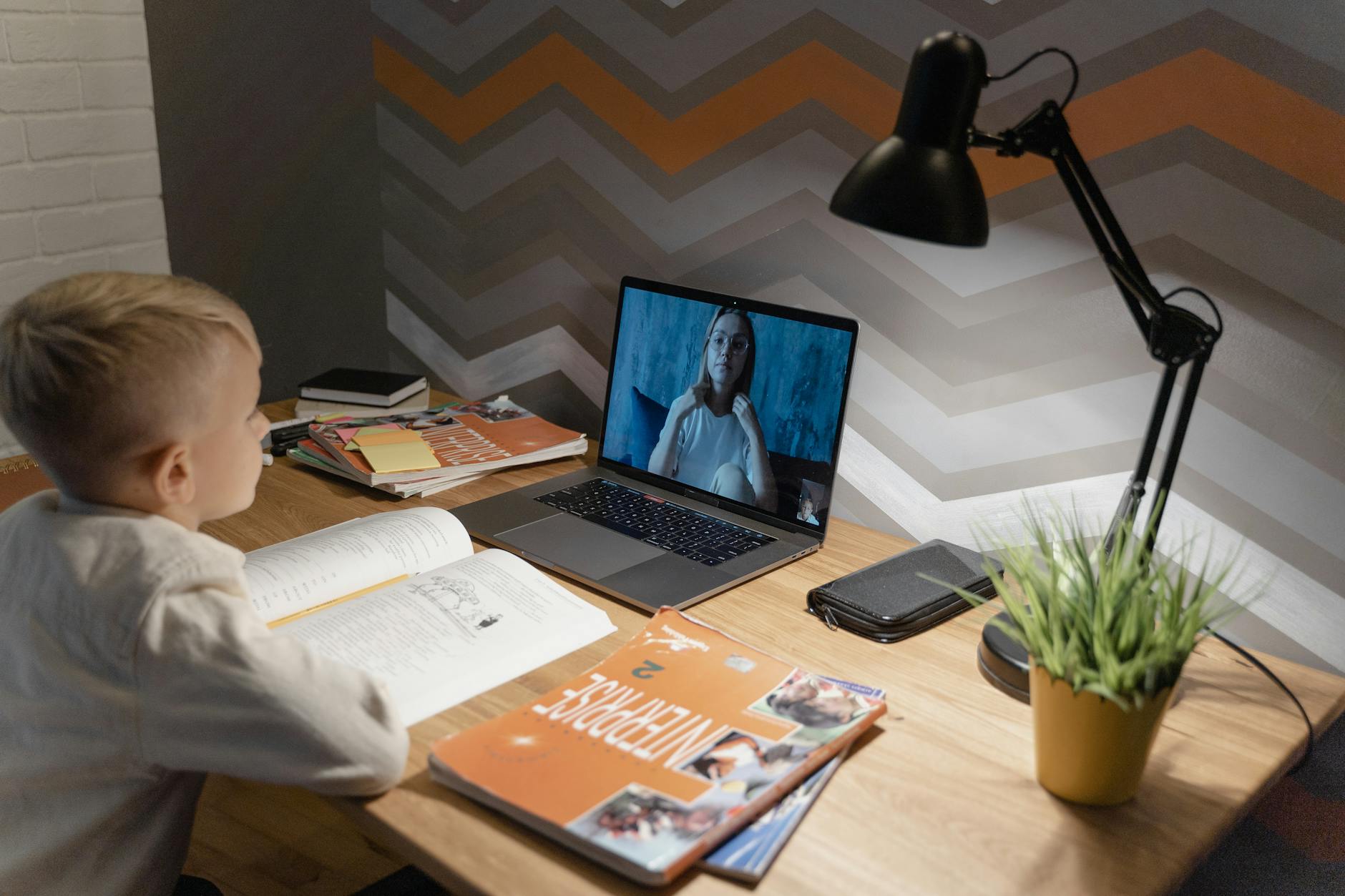 A young boy participates in a virtual class from home, using a laptop and study materials. (Photo by Tima Miroshnichenko on Pexels)