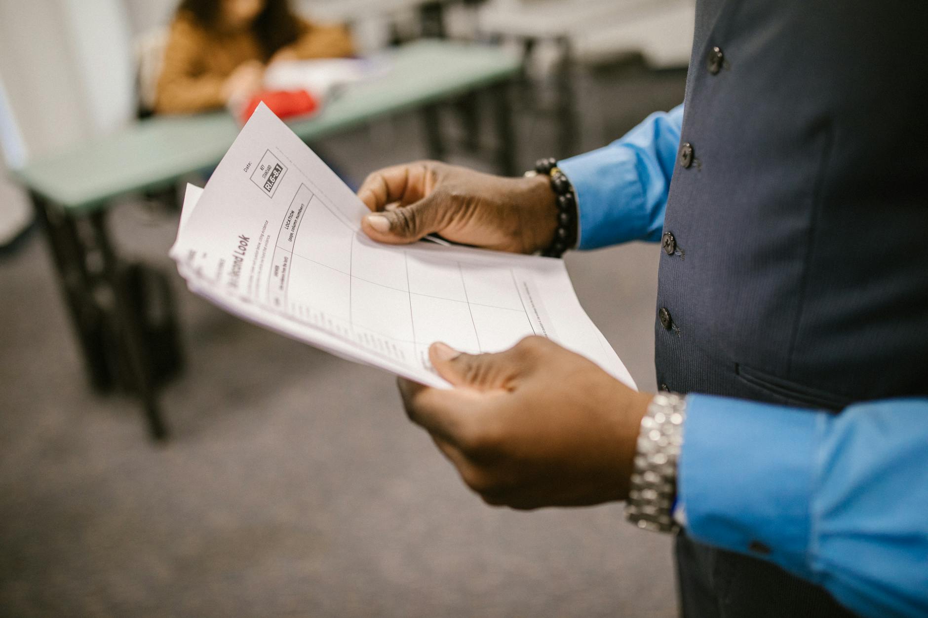 An instructor examining test papers in a classroom setting, focusing on education and evaluation. (Photo by RDNE Stock project on Pexels)