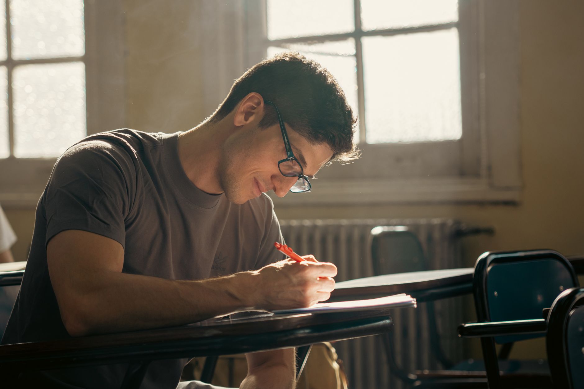 A student concentrating on writing during a class session in a warmly lit university classroom. (Photo by Eduard Perez on Pexels)
