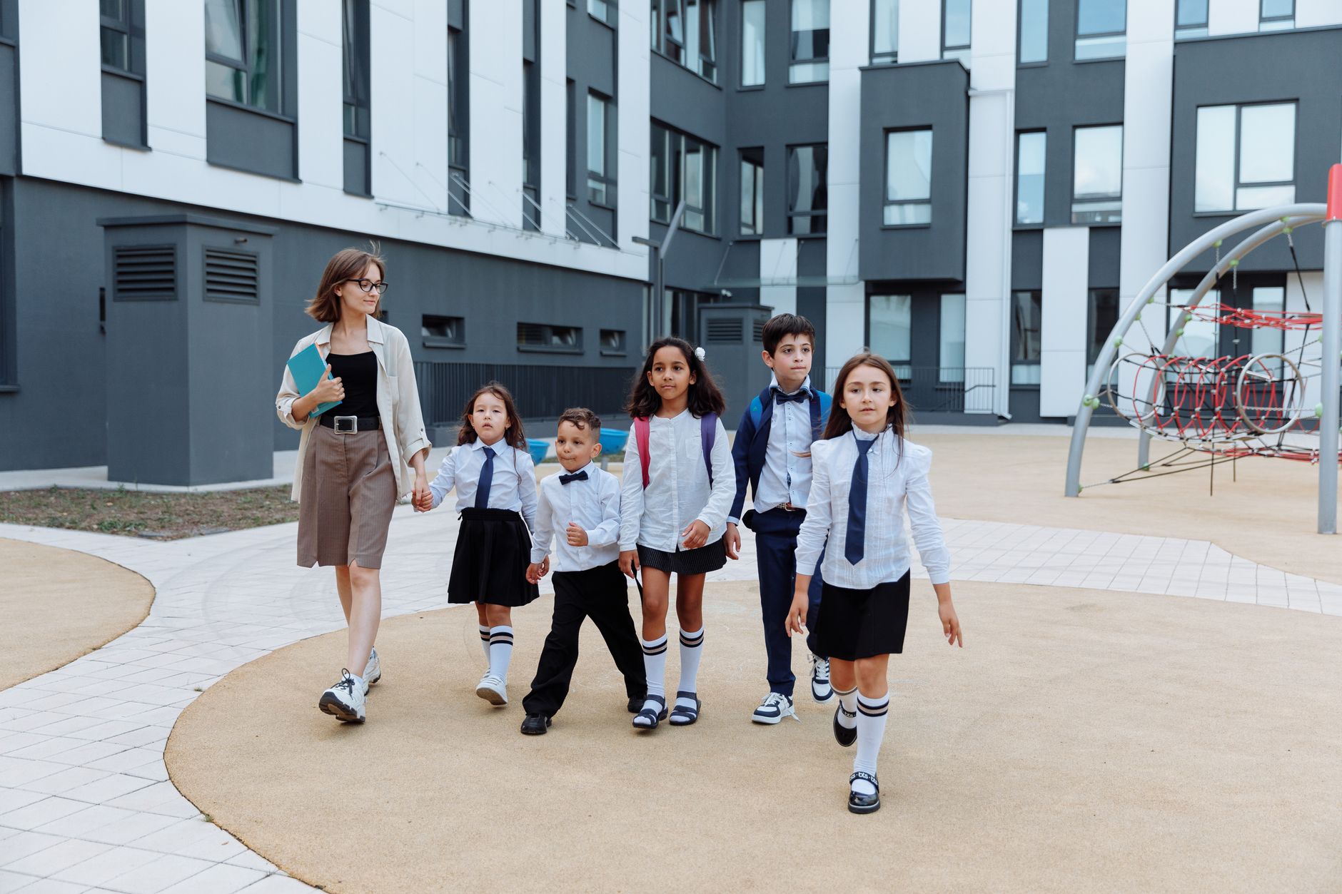 A teacher leading a group of diverse students on a modern school campus walkway. (Photo by Thirdman on Pexels)